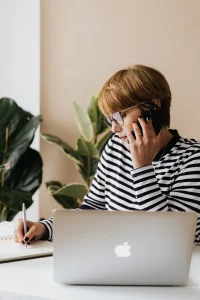 woman speaks on phone while taking notes